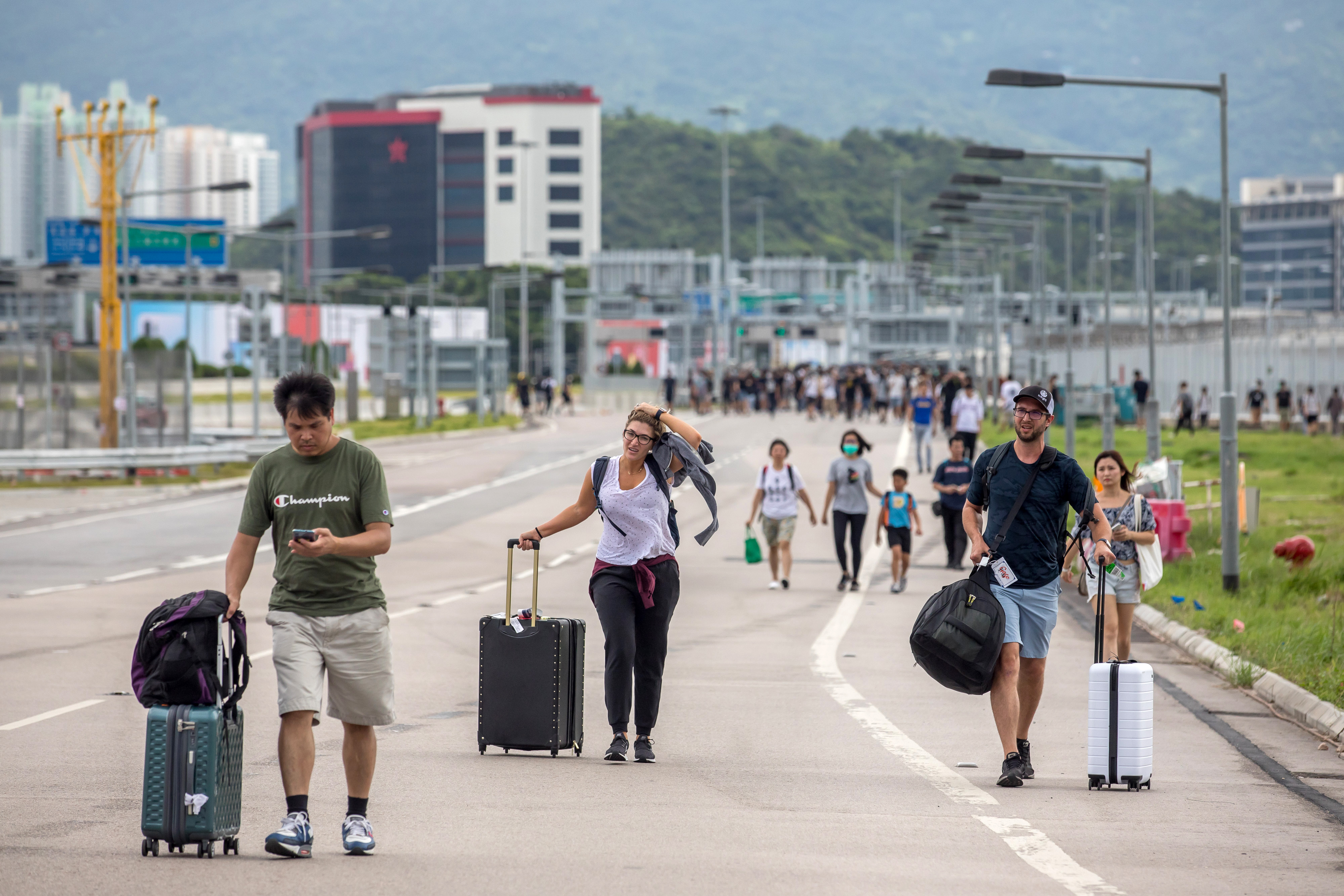 Travelers walk with their luggage along a road towards the Hong Kong International Airport during a protest in Hong Kong, China, on Sunday, Sept. 1, 2019.