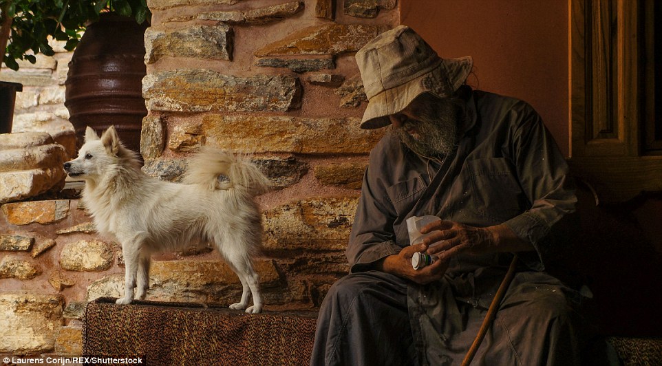 An elder Monk sits by the entrance to the Dochiariou monastery together with one of his dogs
