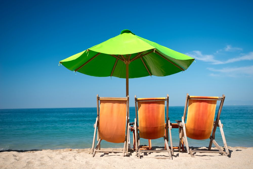 three orange beach chairs and a green umbrella facing the ocean in Puerto Vallarta Mexico